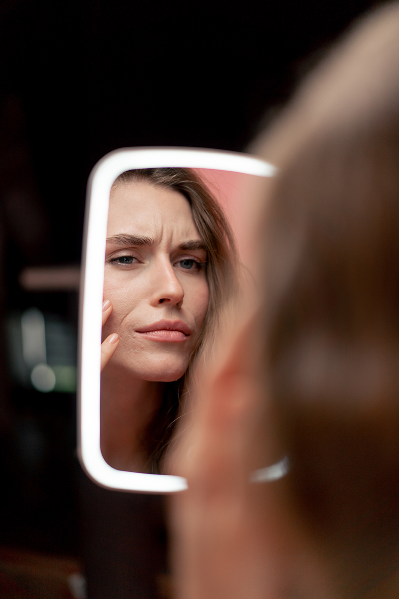 Woman examining her skin in a lit mirror